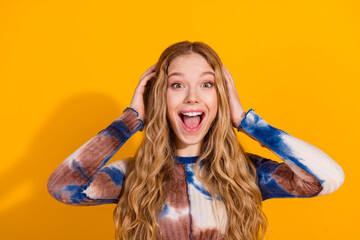 Joyful young woman with long blonde hair in a tie dye shirt poses against a bright yellow background for a vibrant fashion lifestyle stock photo