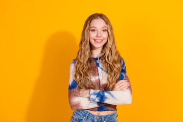 Young woman with long blonde hair wearing tie dye top and jeans stands against a bright yellow background smiling for a fashion lifestyle image