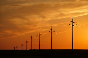 Silhouette of power lines against vibrant orange sunset sky