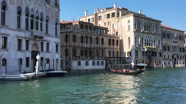 Typical Venetian gondola moving on Grand Canal with historic houses in background in Venice, Italy