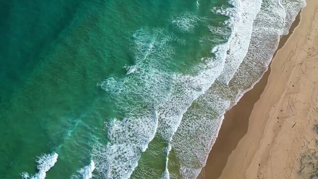 Top down drone view of turquoise ocean waves rolling toward a sandy beach at sunset. White foam patterns meet the shore, creating a calm, natural coastal scene with strong texture, Australia, VIC 