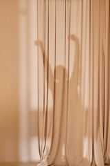 Silhouette of woman stretching behind beige curtains