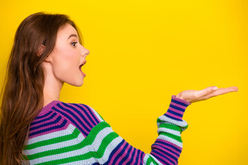 Young woman in colorful striped sweater gesturing toward yellow background in casual fashion scene