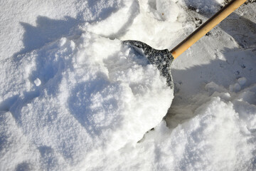 Close up of a snow shovel removing fresh deep snow from a sidewalk on a bright winter day