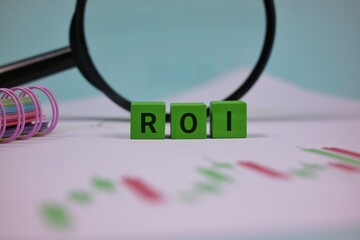 ROI Concept With Green Block Letters and Magnifying Glass Over Financial Paper Symbolizing Investment Analysis. isolated on a turquoise background