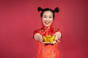 Portrait of smiling woman holding gold yuanbao toward camera on red background