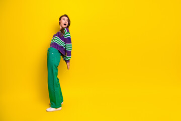 Fototapeta premium Young woman in striped sweater and green jeans poses joyfully against a bright yellow background