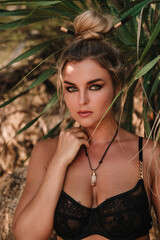 Close-up portrait of confident woman wearing black lace lingerie among tropical palm leaves