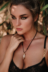 Close-up portrait of confident woman wearing black lace lingerie among tropical palm leaves