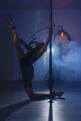 Athletic woman performing pole dance moves in studio with dramatic colored lighting