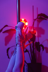 Artistic close-up of pole dance platform shoes and legs on  pole in studio with vibrant pink and purple light