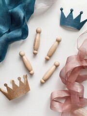 Colorful crowns and wooden figures arranged on a white surface. Decorative ribbons in blue and pink add a festive touch, symbolizing Purim celebrations.