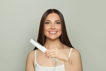 Young woman brunette with long straight smooth hairstyle using hair straightener iron on light grey background