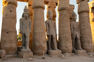Tall stone statues and ancient columns in a temple complex in Luxor at sunset