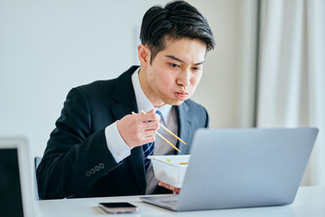 カップ焼きそばを食べながら仕事をする20代の若い男性