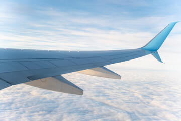 View of airplane wing above clouds during day, showcasing travel experience and distant sky