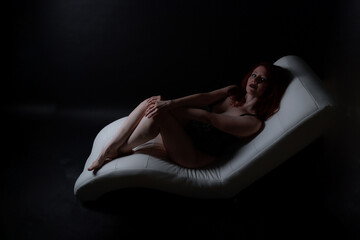 Low-Key-Boudoiraufnahme einer rothaarigen Frau in Lingerie, liegend im Spiel aus Licht und...