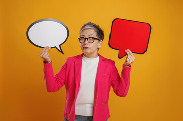 Woman with short gray hair is holding speech bubbles in contrasting colors, showcasing communication concepts and expressions against a vibrant yellow background