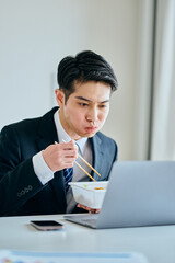 カップ焼きそばを食べながら仕事をする20代の若い男性