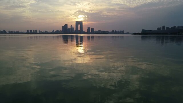 Low angle drone flight over Jinji lake with reflection of silhouettes of the iconic modern Suzhou skyline at sunset, urban and natural landscape China

