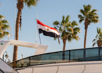 Flag of Egypt waves over a boat in a sunny tropical location surrounded by palm trees