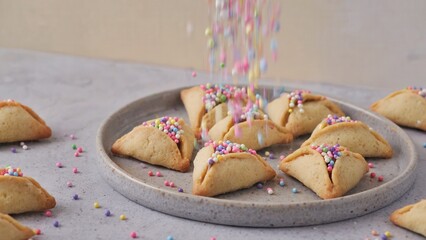 A plate of hamantaschen pastries with colorful sprinkles. The scene captures the festive spirit of Purim, a Jewish holiday celebrated with food and family traditions.
