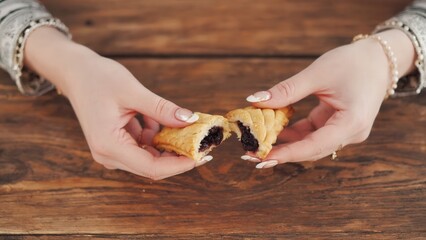 A pair of hands, with manicured nails, breaking a hamantaschen pastry filled with chocolate. The scene captures the joy of Purim celebrations.
