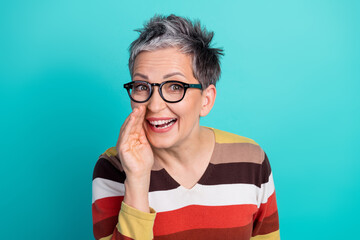 Smiling mature woman with short gray hair wearing glasses and a striped sweater against a blue background