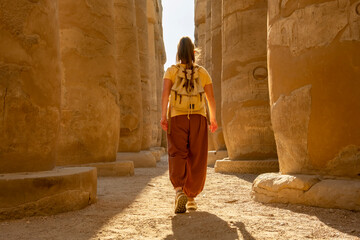 Woman visitor walks through ancient Luxor Temple columns in warm sunlight during afternoon