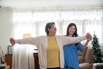 Asian young female caregiver helping senior patient workout exercise with dumbbell at home. Elderly...
