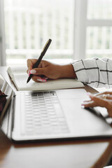 Female writing in notebook while using laptop