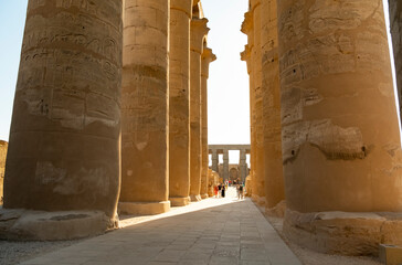 View of tall ancient columns in Luxor temple during sunset with visitors exploring the historical site