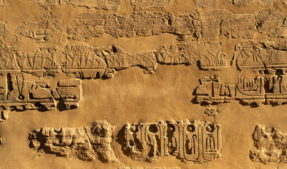 Hieroglyphics on an ancient stone wall in Egypt show scenes of daily life and historical events through carved symbols, Luxor Temple
