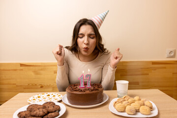 Seventeen year old girl in party hat blowing number seventeen candles on chocolate birthday cake.