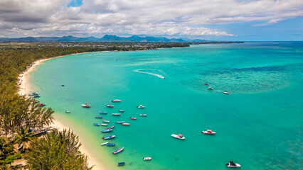 Stunning aerial view of a curved tropical coastline with turquoise lagoon water, numerous motorboats at anchor, and a long sandy beach lined with lush green trees © Yuliko