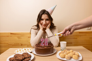 Twenty eight year old woman smiling while another person lights number twenty eight birthday candles.