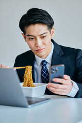 カップ焼きそばを食べながらスマホを操作する20代の若い男性