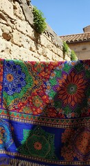 Colorful Textile Displayed Against Stone Wall in Italian Village.