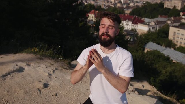 Yoga self-care, Scenic yoga, Yoga meditation. Clad in white and black, young man balances on one leg atop hill on yoga mat, promoting mindfulness and healthy living outdoors.