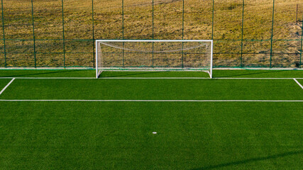Football goal on artificial turf with fence and training field background