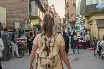 Tourist walks through busy market in Luxor, Egypt, exploring shops and local culture in the evening light with a backpack