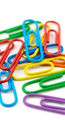 Colorful paperclips scattered on a white surface, office supplies.