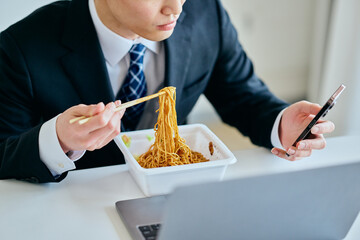 カップ焼きそばを食べながらスマホを操作する20代の若い男性