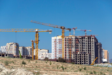New residential district under construction in Novorossiysk, Russia, with unfinished monolithic apartment buildings and tower cranes against the sky