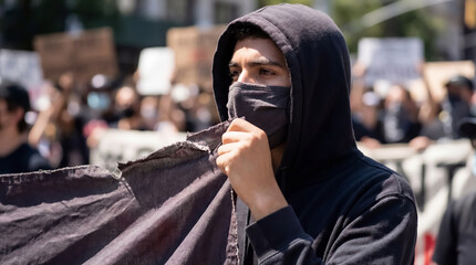 Close-up of an activist with a determined look standing on the street against a blurred background of people with placards during a demonstration