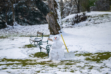 A snowman with a snow shovel is standing in a park