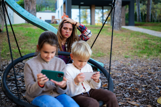 Mother feeling frustration and worry as her children are absorbed by their mobile phones, highlighting the challenge of screen time and modern parenting in a family outdoor setting