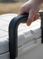 Hand gripping textured handle of a white portable cooler outdoors on a sunny day.