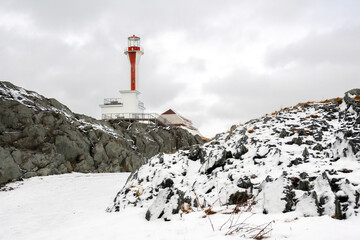 Cape Forchu Lighthouse surrounded by fresh snow and rugged rocky terrain. A serene winter coastal scene highlighting the landmark in a frozen landscape.
