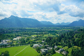 High-angle aerial view of the lush green valley and Alps mountains in Salzburg, Austria, on a cloudy summer day